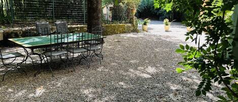 An outdoor dining area with a table and chairs, surrounded by gravel and greenery.