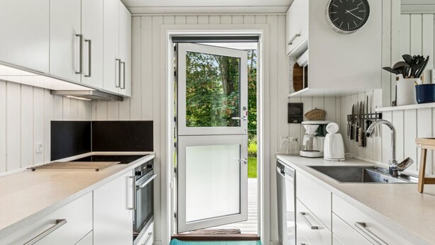 Une cuisine moderne avec des meubles blancs, une grande fenêtre et une vue sur la verdure.