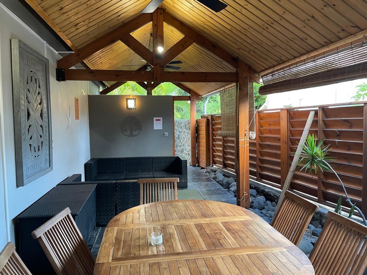 A covered outdoor seating area with a round wooden table and cushioned seating.