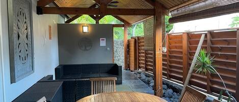 A covered outdoor seating area with a round wooden table and cushioned seating.
