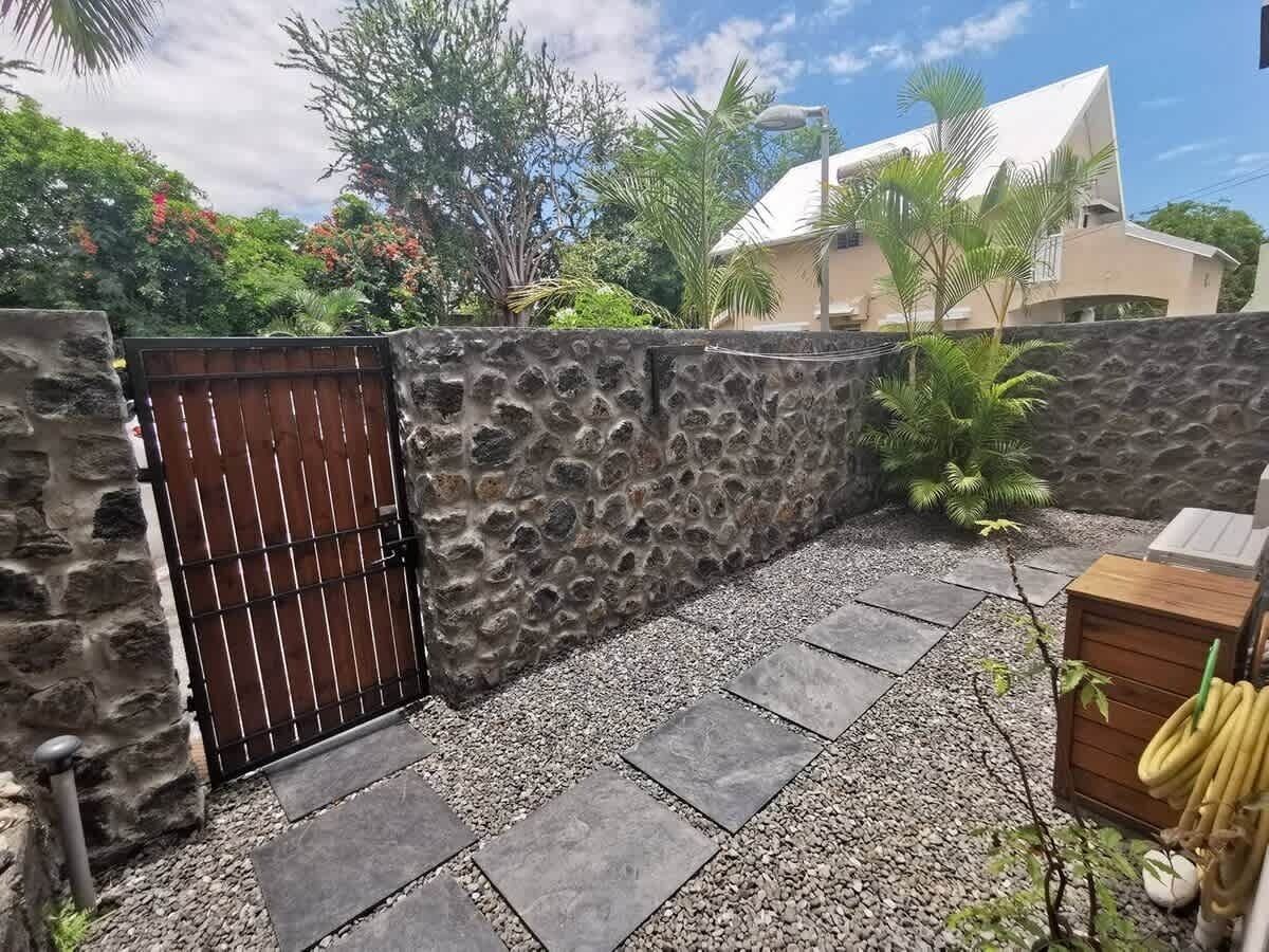 A stone wall with a metal gate, a paved patio, and a wooden bench.