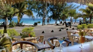 Un espace extérieur aménagé pour les repas, avec des tables et des chaises, offrant une vue sur une plage et l’océan.