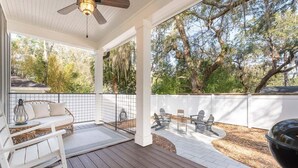 A covered outdoor patio with a seating area, a grill, and a view of trees.
