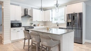A modern kitchen with white cabinetry, a stainless steel refrigerator, and a central island with bar stools.