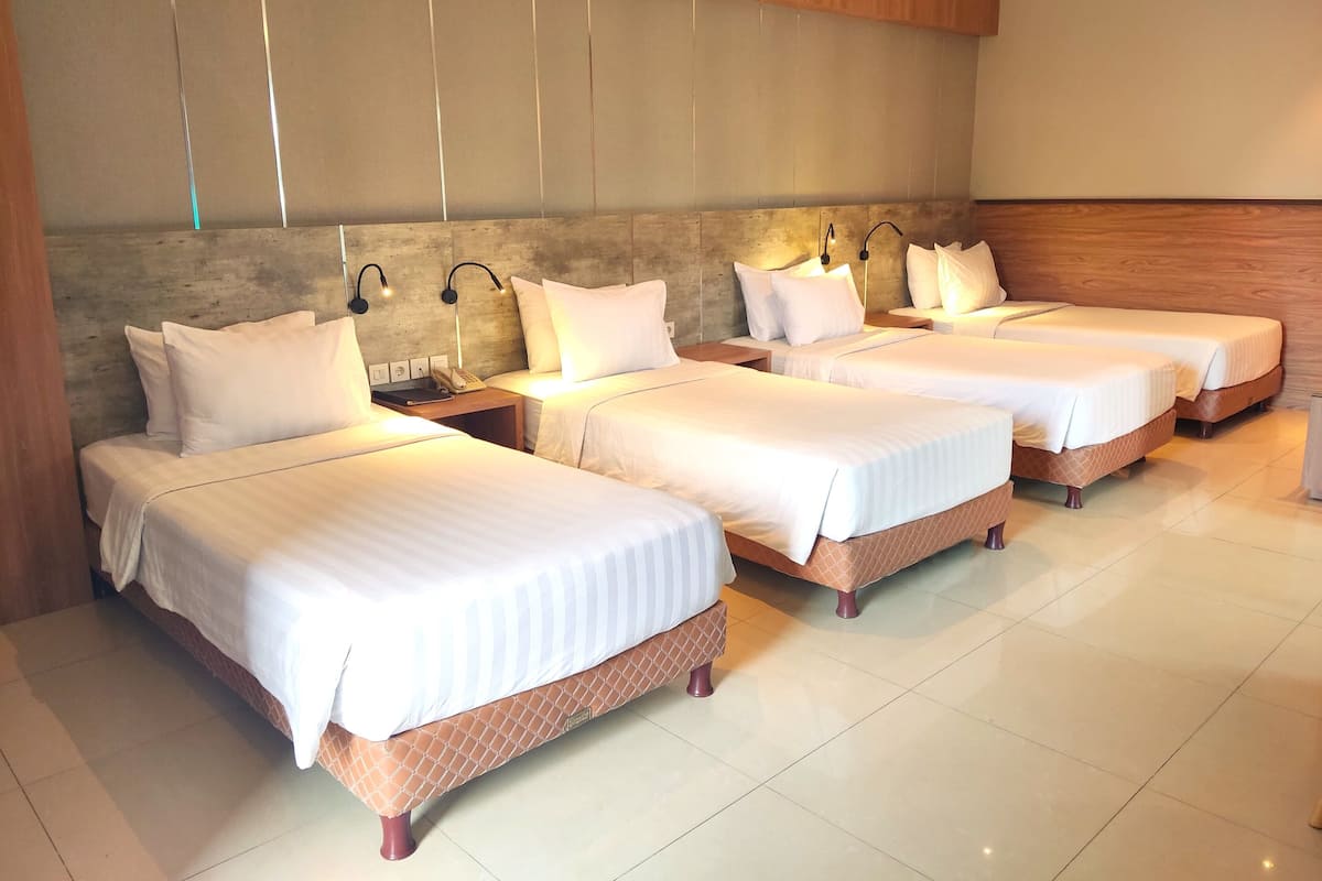 Habitación de hotel con cuatro camas dispuestas en fila, cada una con ropa de cama blanca y cabeceros de madera.