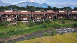 A row of hotel buildings with balconies overlooking a river and mountains in the background.