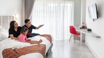 A modern hotel room with a bed, a TV mounted on the wall, a desk with a chair, and a window with curtains.