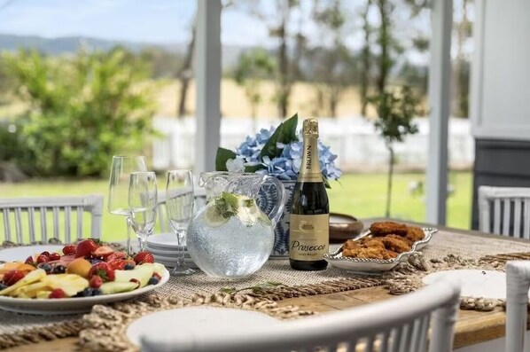 Een gedekte tafel voor een maaltijd, met een fles Prosecco, een waterkan en een schaal fruit.
