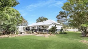 A white house with a covered porch, surrounded by a well-maintained lawn and trees. - The Dawning Farmhouse (Jaspers Brush)