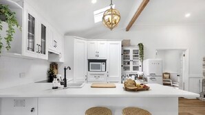 A modern kitchen with white cabinetry, a central island with stools, a hanging light fixture, and a microwave. - The Dawning Farmhouse (Jaspers Brush)