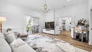 A spacious living room with a large sofa, a TV, and a chandelier. There is a sliding glass door leading to a balcony. - The Dawning Farmhouse (Jaspers Brush)