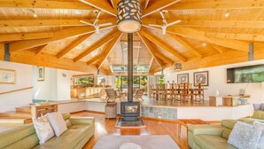 A spacious living area with a high ceiling, a fireplace, and a dining area with multiple chairs. - Osprey Lodge - Bungalow & House (Eaglehawk Neck)