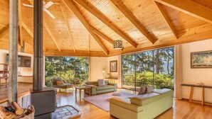 A spacious living room with a large wooden ceiling, a fireplace, and a view of the outdoors. - Osprey Lodge - Bungalow & House (Eaglehawk Neck)