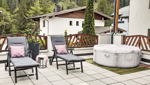 A terrace with two lounge chairs, a small table, and a round ottoman. - Sandra Falch by Interhome (Flirsch)