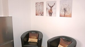 A room with two black leather chairs, each with a patterned cushion. There are three framed pictures on the wall. A stainless steel refrigerator is visible on the left. - Sandra Falch by Interhome (Flirsch)