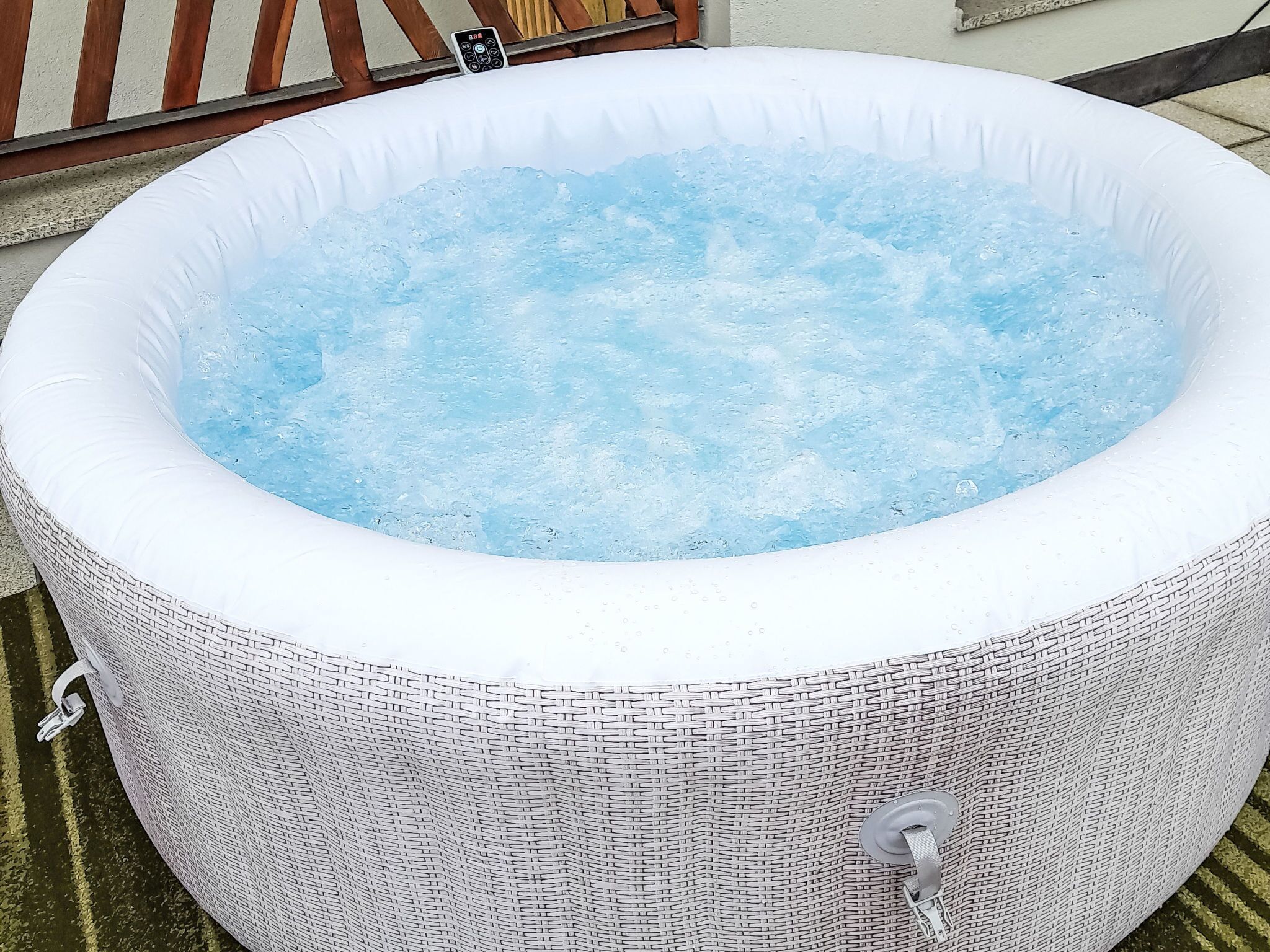Un grand jacuzzi gonflable doté d’un panneau de commande sur le dessus, entouré d’une clôture en osier.