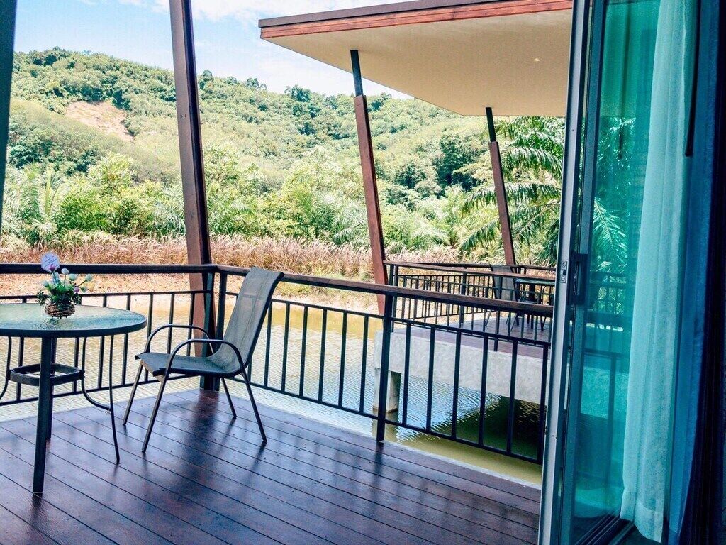 A balcony with a table and chairs, a glass door, and a view of a lush green landscape.