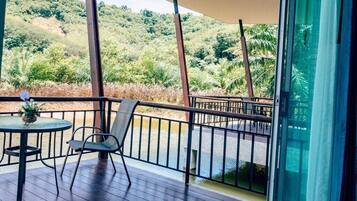 A balcony with a table and chairs, a glass door, and a view of a lush green landscape.