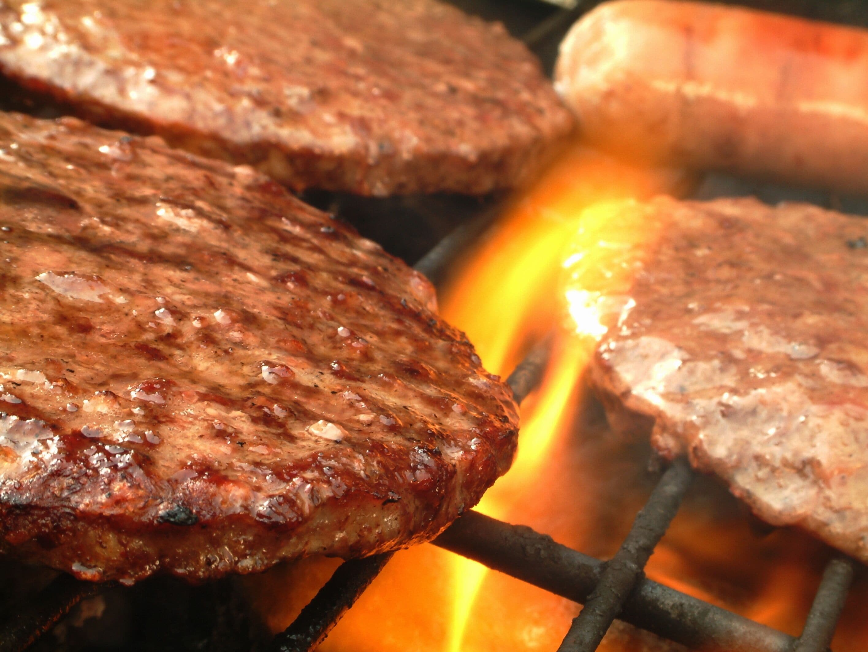 Three grilled hamburgers on a grill with visible flames.
