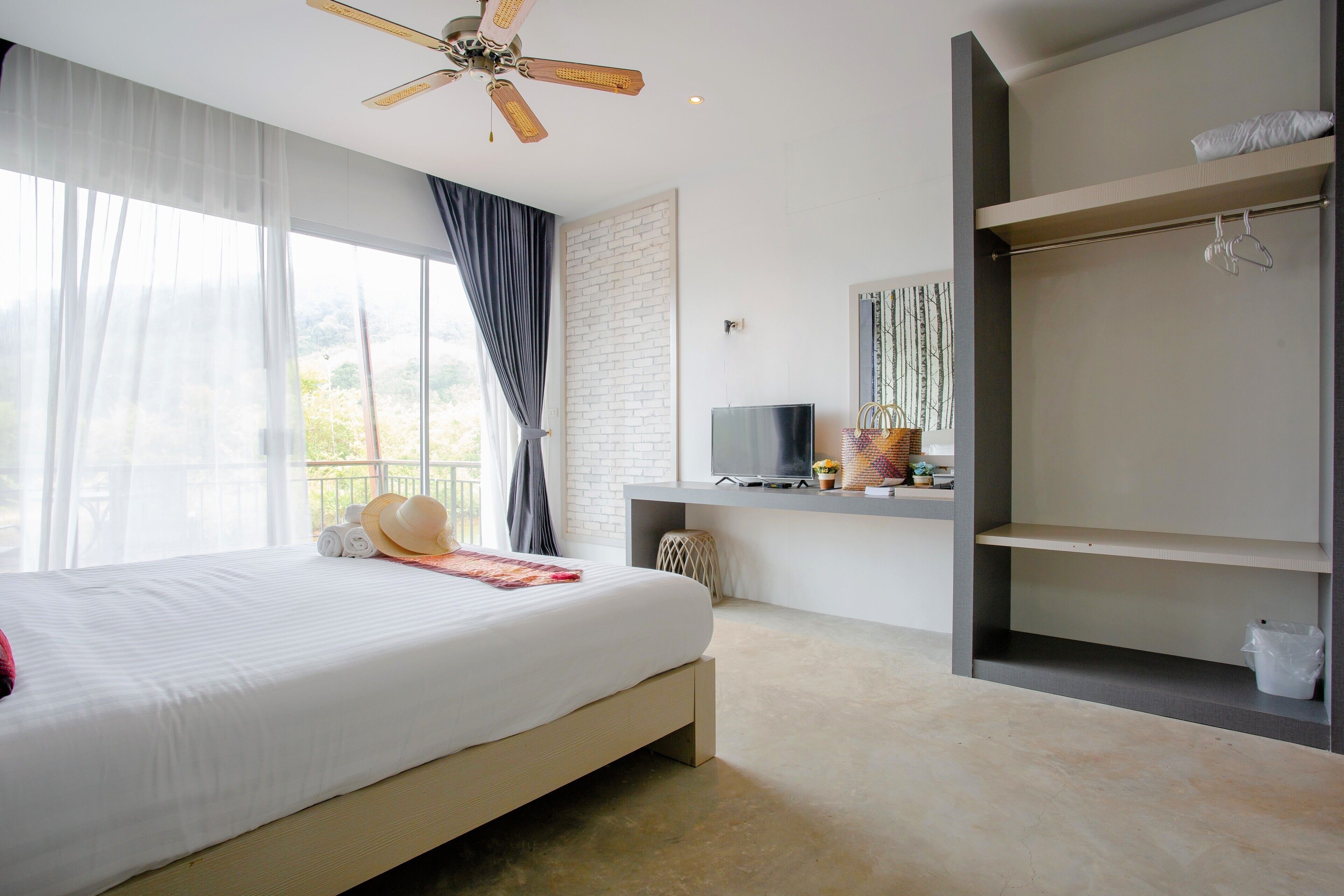 Una habitación de hotel moderna con una cama grande, un escritorio con un televisor de pantalla plana, un armario y un ventilador de techo.