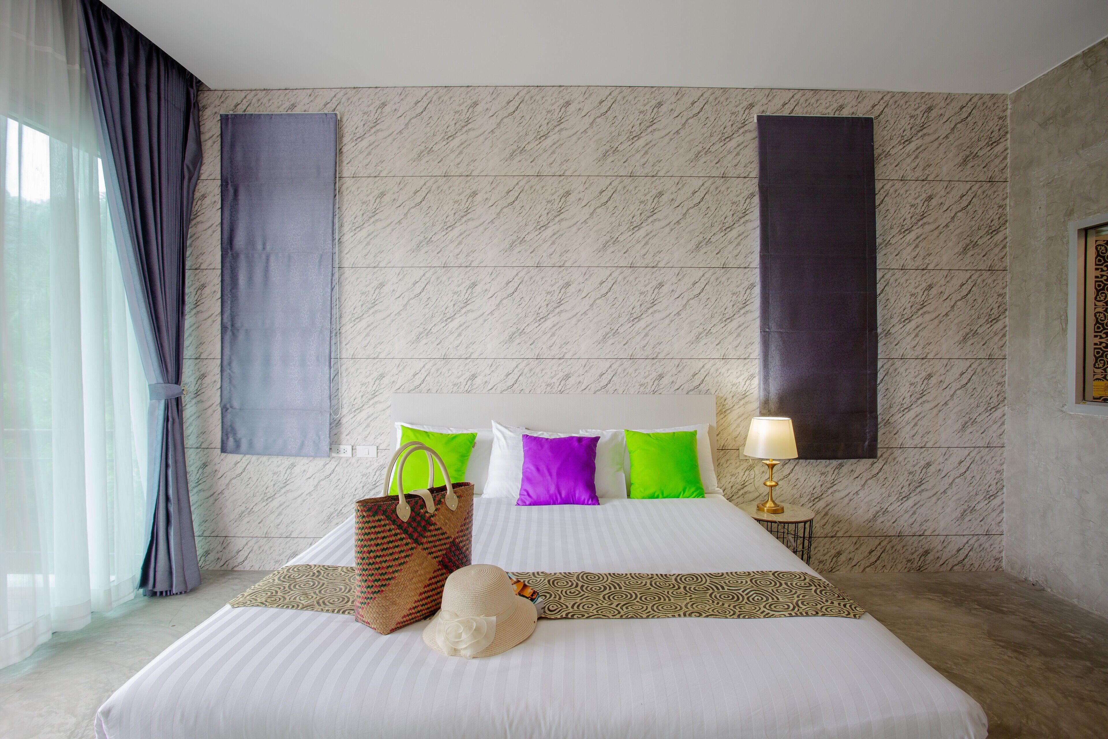 A hotel room with a large bed, a headboard, a bedside table with a lamp, and a window with curtains.
