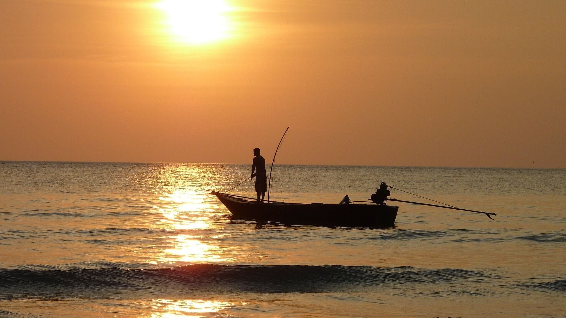 A boat with two people on a calm sea at sunset.