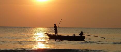 A boat with two people on a calm sea at sunset.