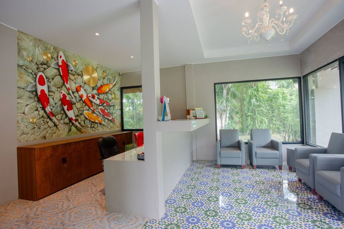 A modern interior with a reception desk, seating area, and large windows offering a view of greenery.