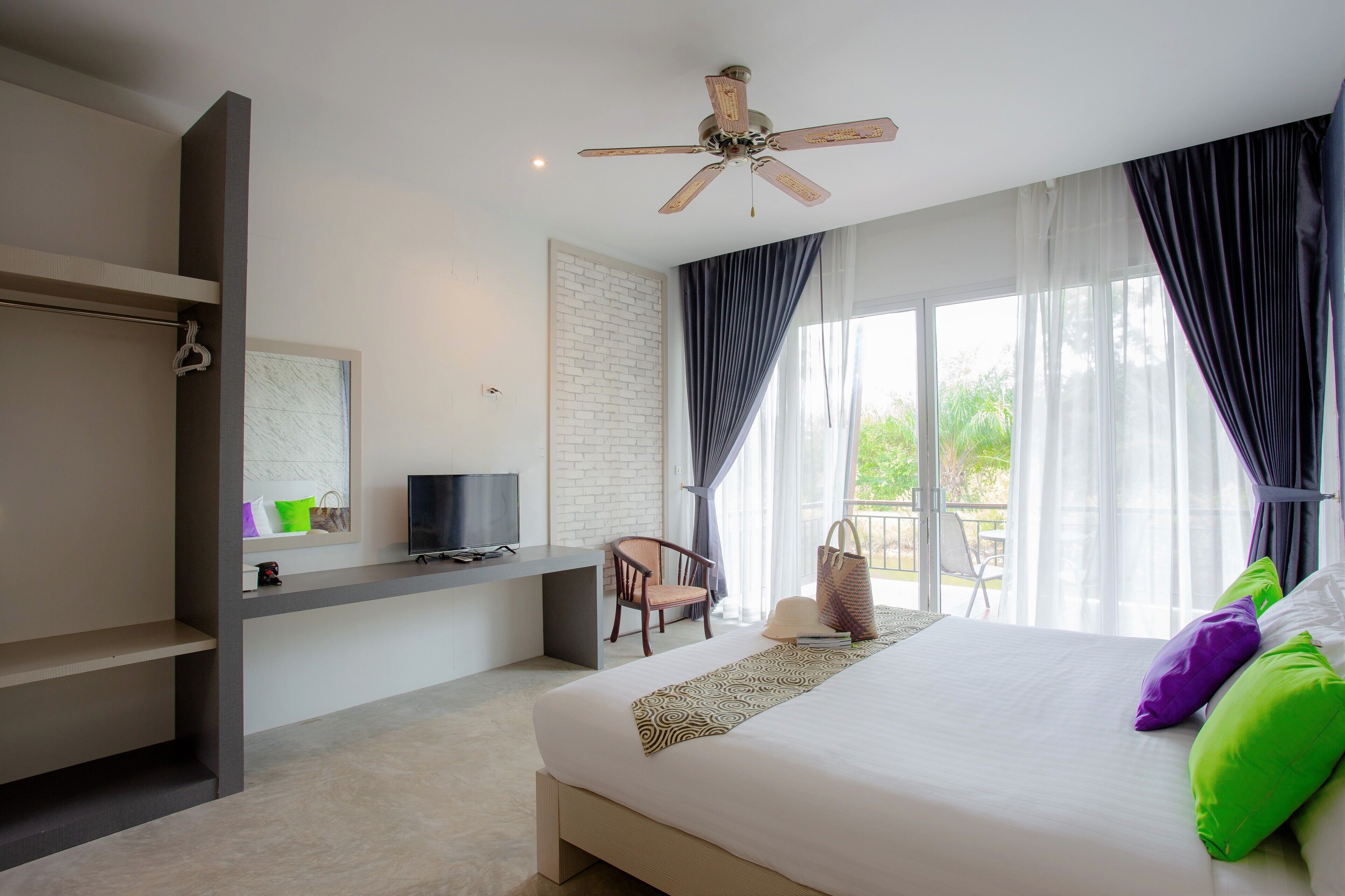 A modern hotel room with a large bed, a desk with a TV, a chair, and a balcony with curtains.