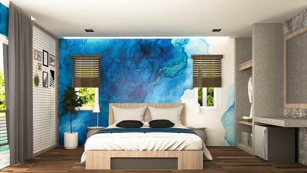 Une chambre moderne avec un grand lit, un mur bleu orné d’une œuvre abstraite et un banc intégré.