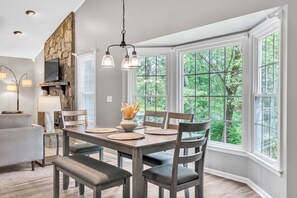 A dining area with a stone accent wall, a television, and a large window with a view of trees. - Pet-Friendly 5BR Getaway near Lake Keowee (Seneca)