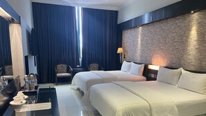 Hotellihuone, jossa on kaksi sänkyä, työpöytä lampun kanssa, tuoli ja suuri ikkuna, josta on näkymä ulos.