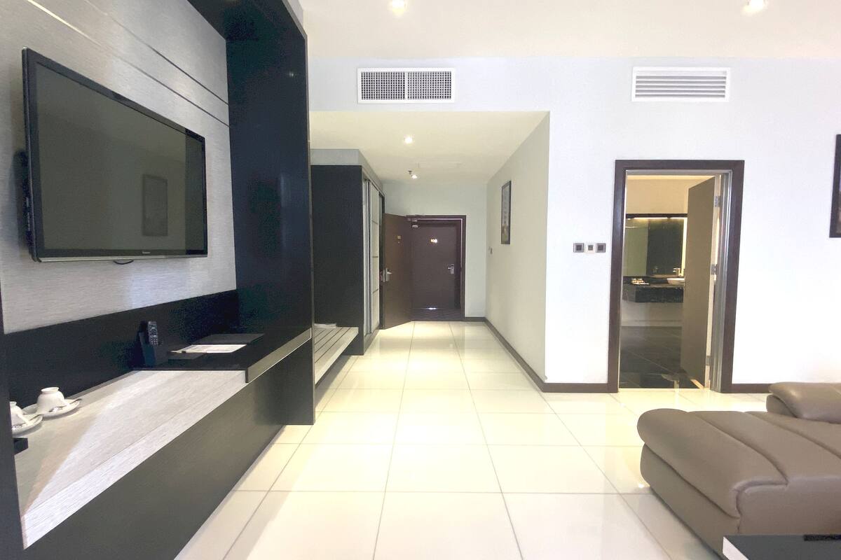 A modern hotel room with a flat-screen TV mounted on the wall, a built-in sink, and a sofa.