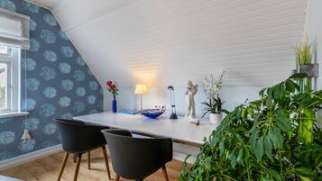 A dining area with a white ceiling, a blue floral wallpaper, a table with chairs, a lamp, and decorative items.