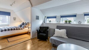 A loft-style bedroom with a loft bed, a gray sofa, a black armchair, and a window with a view. - Apartment "Schwennautal" with Private Garden & Wi-Fi (Glücksburg)