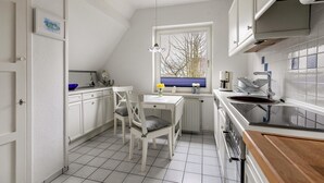 A kitchen with white cabinets, a dining table with chairs, a window with a view, and a stove. - Apartment "Schwennautal" with Private Garden & Wi-Fi (Glücksburg)