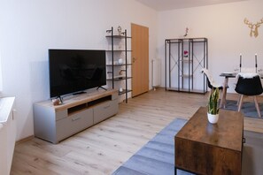 Un salon moderne doté d’un téléviseur à écran plat, d’un parquet, d’un meuble de rangement gris, d’une chaise noire et blanche et d’une petite table avec des bougies.