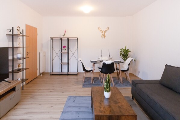 Un salon comprenant un canapé, une table basse, un meuble pour la télévision et un coin repas avec des chaises et une table.