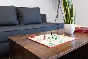 Un jeu de société sur une table en bois, avec un canapé et une plante en pot en arrière-plan.