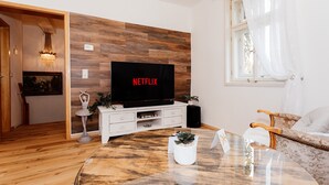 Un soggiorno con parete in legno, televisione, divano bianco, tavolino da caffè e finestra con tende.