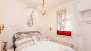 Una camera da letto con un letto, un lampadario, uno specchio, una finestra con persiane rosse e un attaccapanni a parete.