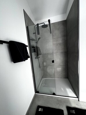 A modern shower room with a glass door, a towel rack, and a shower head.