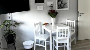 A dining area with a white table and chairs, a flat-screen TV mounted on the wall, and a door to the right. - Studio Apartment 'Lorenz' with Wi-Fi (Olching)