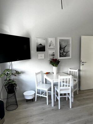 Un comedor con una mesa y sillas blancas, un televisor de pantalla plana en la pared y una puerta a la derecha.