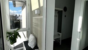 A modern room with a glass door leading to a balcony, a white chair, a potted plant, and a white cabinet. - Studio Apartment 'Lorenz' with Wi-Fi (Olching)