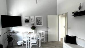 A minimalist living room with a dining area, a flat-screen TV, a sofa, and a door leading to another room. - Studio Apartment 'Lorenz' with Wi-Fi (Olching)