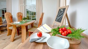 Una mesa de madera para comer con un posavasos verde, un plato blanco con un tomate, un cuchillo, un cuenco blanco y una pequeña pizarra con la palabra 'Welcome'.