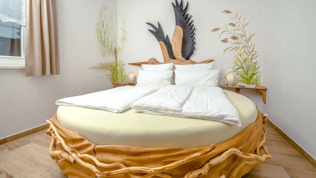 Una cama con un original cabecero de madera, una escultura de pájaro en la pared y una planta junto a la cama.