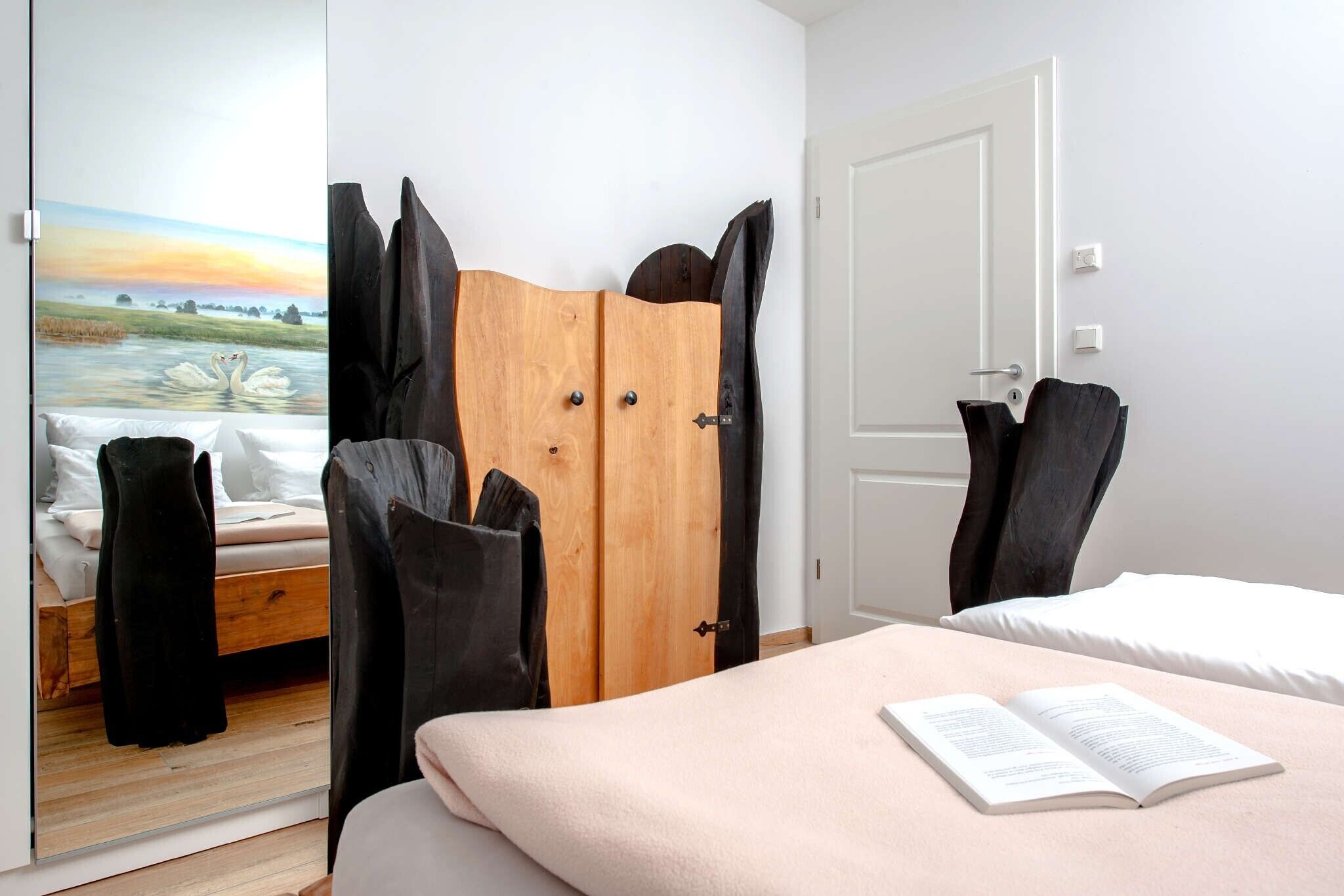 A bedroom with a bed, a wooden wardrobe, a door, and a painting of swans on the wall.