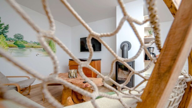 Ein Hängestuhl, ein Holztisch, ein Fernseher und ein Kamin in einem Raum mit einem Landschaftsgemälde.